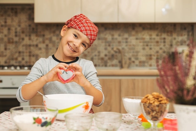 Cute boy shef mostrando su amor mientras cocina sosteniendo un corazón para galletas