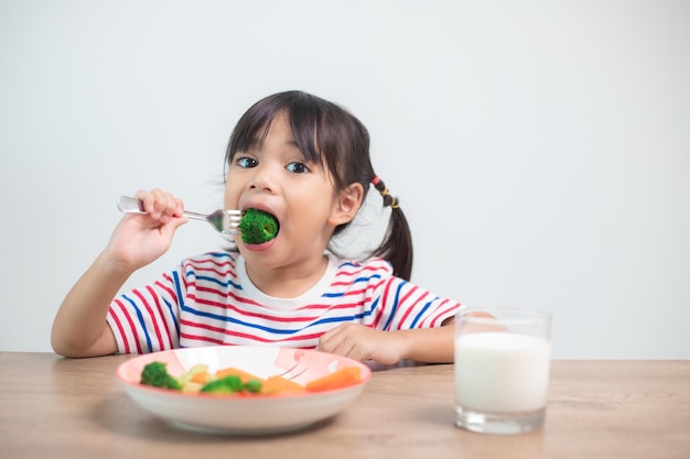 Cute, criança asiática, menina, comer, legumes saudáveis, e, leite, para, dela, refeição