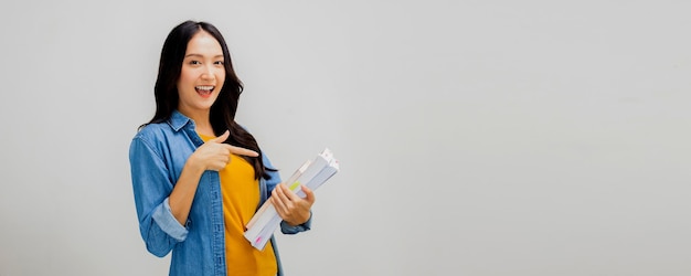 Cute e bela estudante asiática confidencial mulher sorrindo segurando um livro de papel positivo natural linda adolescente tailandesa em jeans e camisa amarela isolado no estúdio