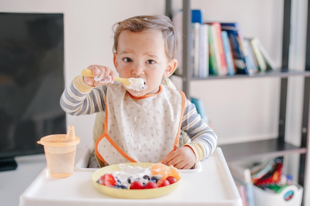 Cute kaukasische Baby Junge isst reife Beeren und Früchte mit Joghurt lustig lächelndes Kind Kind