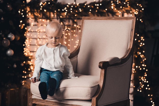 Cute kid girl vistiendo ropa casual sentado en una silla sobre las luces de Navidad