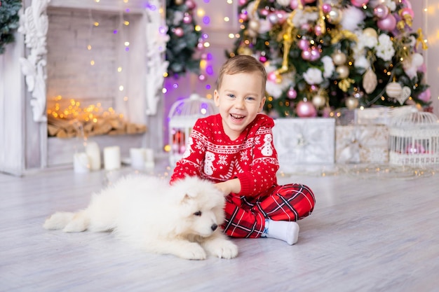Cute Little Baby Boy con un cachorro de Samoyedo blanco cerca del árbol de Navidad, concepto de vacaciones, Año Nuevo