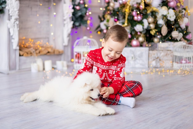 Cute Little Baby Boy con un cachorro de Samoyedo blanco cerca del árbol de Navidad, concepto de vacaciones, Año Nuevo