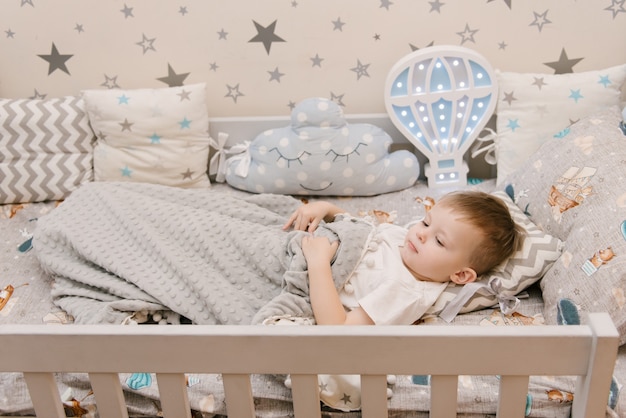 Cute Little Baby Boy sentado en la habitación de los niños en una cama de madera