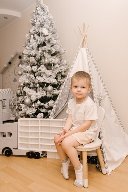 Cute Little Baby Boy sentado en la habitación de los niños en una cama de madera