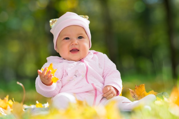 Cute Little Baby Girl en rosa jugando con coloridas hojas amarillas en un parque de otoño en una vista de ángulo bajo contra árboles del bosque