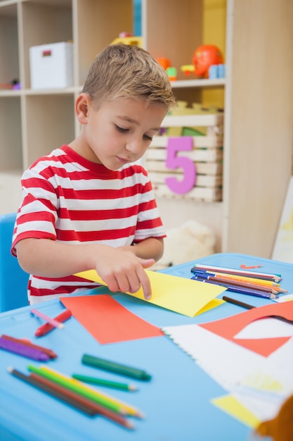 Cute little boy dobrando formas de papel na sala de aula