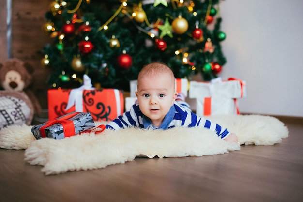 Cute little boy con regalo en decoración navideña Niño en camisa azul blanca tendido sobre una alfombra blanca