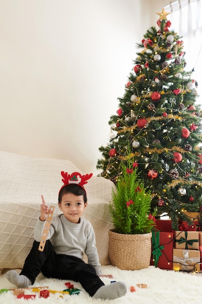 Cute little boy sentado en el suelo en el árbol de navidad y jugando con juguetes