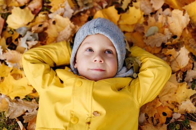 Cute little boy tendido en el suelo cubierto de hojas amarillas caídas