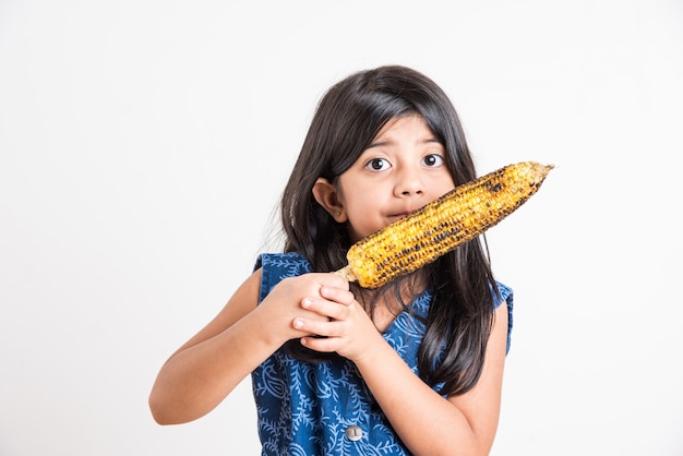 Cute Little Girl India comiendo maíz a la parrilla o Bhutta, que se encuentran aisladas sobre fondo blanco.