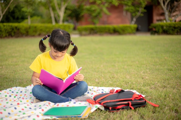 Cute Little Girl libro de lectura afuera sobre el césped