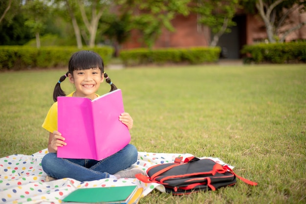 Cute Little Girl libro de lectura afuera sobre el césped