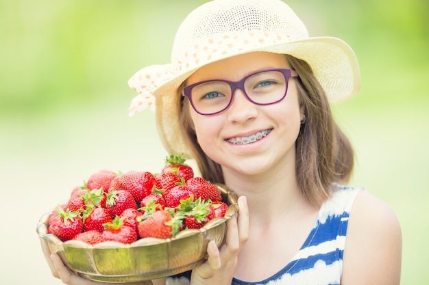 Cute Little Girl con tazón lleno de fresas frescas Pre jovencita con dientes aparatos dentales