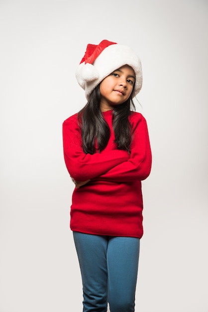 Cute Little Indian Asian Girl vistiendo gorro de Papá Noel celebrando la Navidad mientras se encuentran aisladas sobre fondo liso