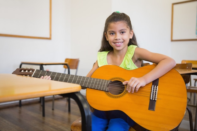 Foto cute pupila tocando violão na sala de aula