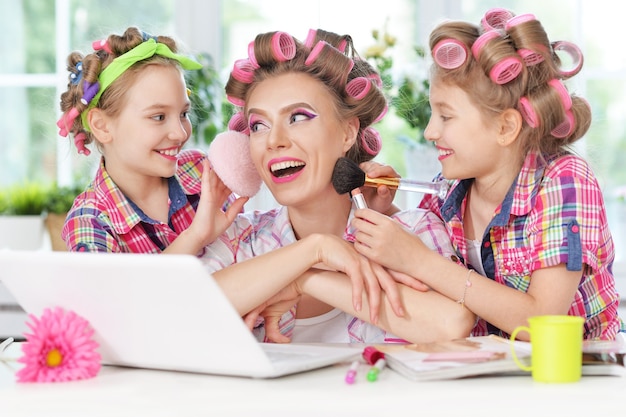 Cute tweenie girls y madre en rizadores de pelo con portátil en casa