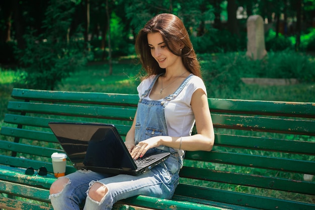Cutie Brunettemädchen, das draußen im Park mit Laptop arbeitet