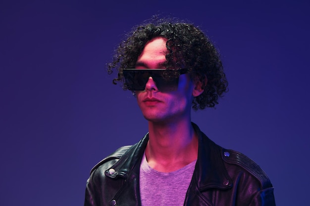 Cyberpunk estilo curly homem casaco de couro óculos de espelho olha para o lado posando isolado em cor rosa fundo azul estúdio oferta de moda legal enorme venda sazonal novo conceito de coleção anúncio de espaço de cópia