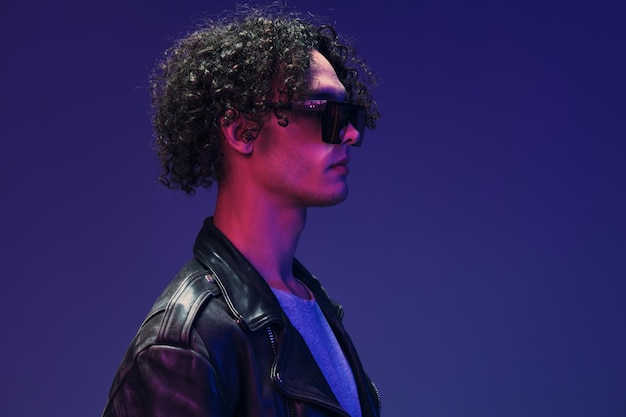 Cyberpunk estilo curly homem casaco de couro óculos de espelho olha para o lado posando isolado em cor rosa fundo azul estúdio oferta de moda legal enorme venda sazonal novo conceito de coleção anúncio de espaço de cópia