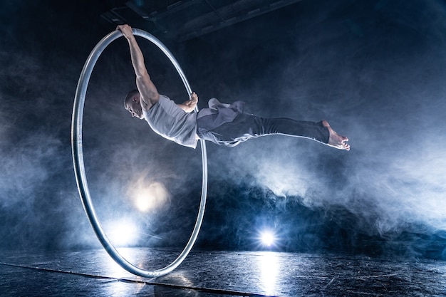 Cyr Wheel Zirkuskünstler auf geräuchertem, dunklem Hintergrund, der auf der Bühne auftritt