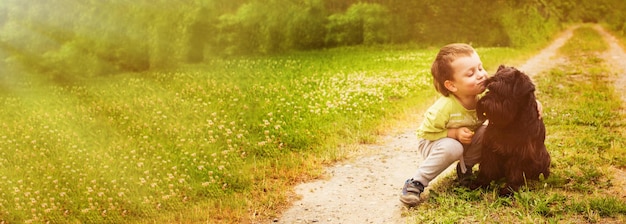 Cyte garotinho com um cachorro andando no parque de verão Criança brincando com o cachorro na natureza Banner