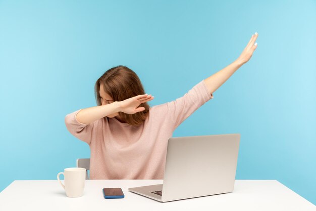 Dabbing tendências. mulher muito feliz mostrando gesto de dança dab, realizando meme de sucesso na internet, sentado no local de trabalho com laptop, trabalho de escritório em casa. tiro de estúdio interno isolado em fundo azul