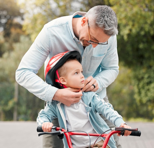 Dad sagt, dass ich immer in Sicherheit sein sollte. Aufnahme eines kleinen Jungen, der auf seinem Fahrrad sitzt, während sein Vater seinen Helm bindet.