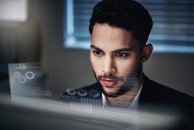 Dados são minha segunda língua Foto de um jovem empresário bonito sentado sozinho no escritório à noite e usando seu computador