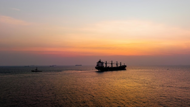 Dämmerung des Meereslandschafts und Silhouette des Containerschiffs, das im Meer und über dem Sonnenlicht-Hintergrund schwimmt