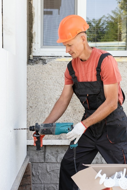 Dämmung des Hauses mit Polyschaum. Der Arbeiter bohrt Löcher, um die Styroporplatte an der Fassade zu befestigen.