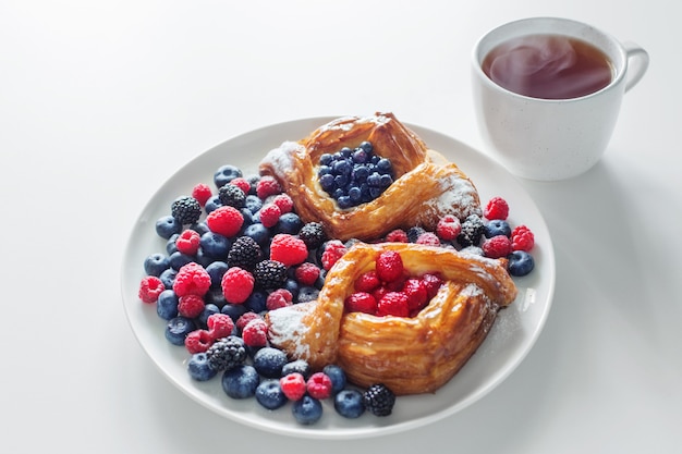 Dänisch mit Himbeeren und Blaubeeren mit Tasse Tee auf weißem Tisch