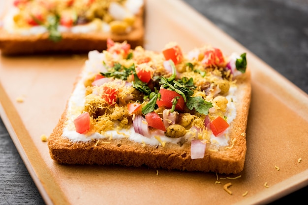 Dahi Bread papdi chaat, chat ist eine leckere Vorspeise oder Vorspeise aus Indien, serviert auf einem mit Tomaten, Sev und Koriander und Masala garnierten Teller. selektiver Fokus