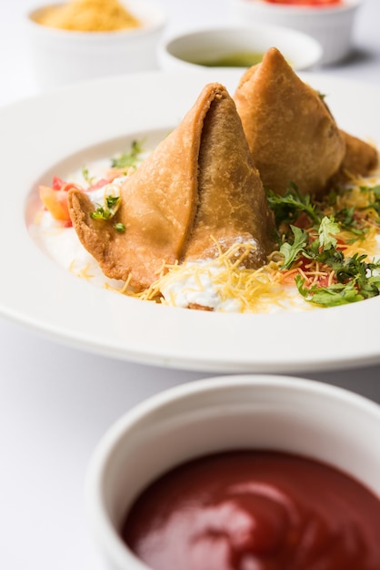 Dahi Samosa o samosa es un bocadillo popular del norte de la India bañado en cuajada, comida chatarra favorita a la hora del té servida con tamarindo y salsa picante de menta o salsa de tomate y chile verde frito.