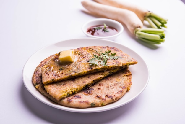 Daikon oder Rettich oder Mooli gefüllte Paratha serviert in einem Teller mit Butter und Tomatenketchup, über buntem oder hölzernem Hintergrund. selektiver Fokus