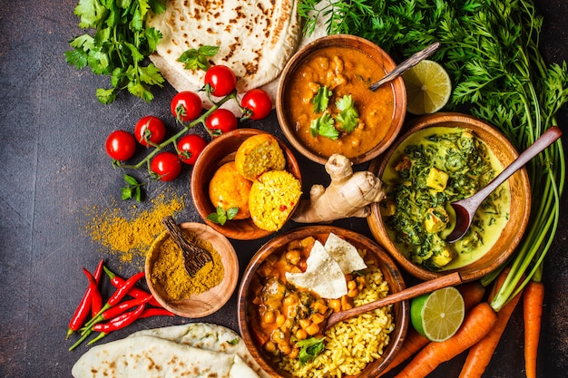 Dal, palak paneer, curry, arroz, chapati, chutney en cuencos de madera en la mesa oscura.