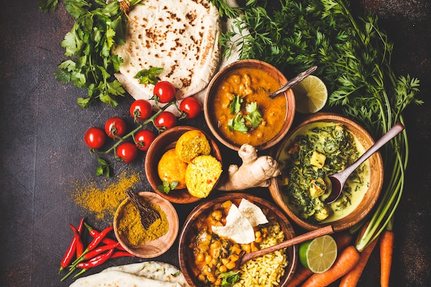 Foto dal, palak paneer, curry, arroz, chapati, chutney en cuencos de madera en la mesa oscura.