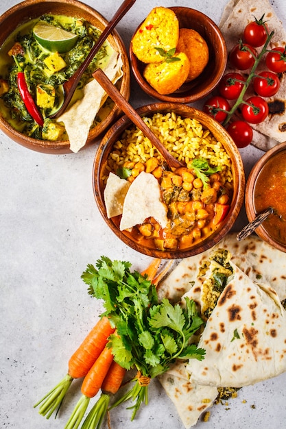 Dal, palak paneer, curry, arroz, chapati, chutney en cuencos de madera sobre la mesa blanca.