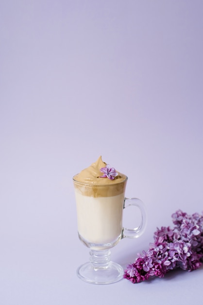 Dalgona linda beber um café espumoso em uma caneca transparente e flores lilás para roxo Il fundo roxo