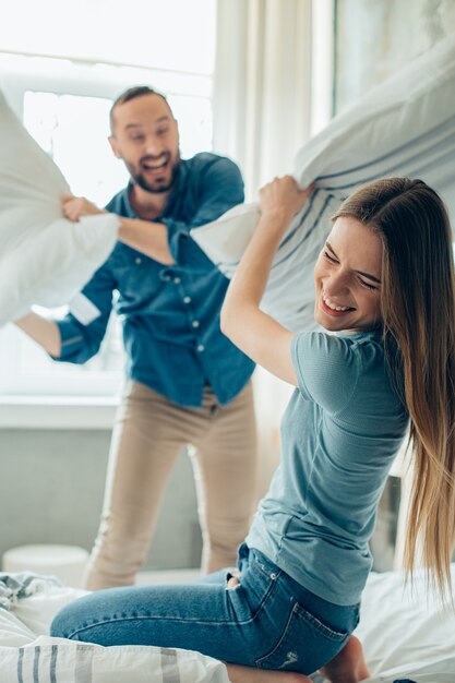 Dama alegre disfrutando de una divertida pelea de almohadas con un novio durante la cuarentena