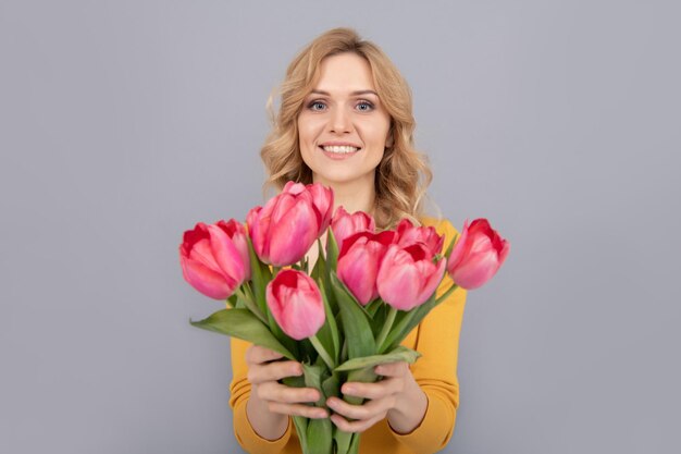 Una dama alegre sostiene flores para las vacaciones de primavera con un fondo gris. enfoque selectivo