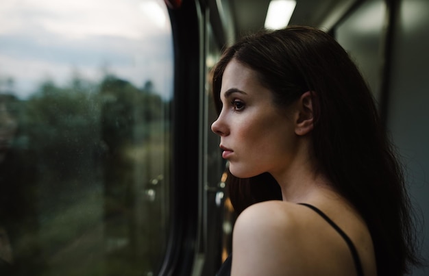 Una dama atractiva mira por la ventana del tren con una cara pensativa en un hermoso paisaje nocturno