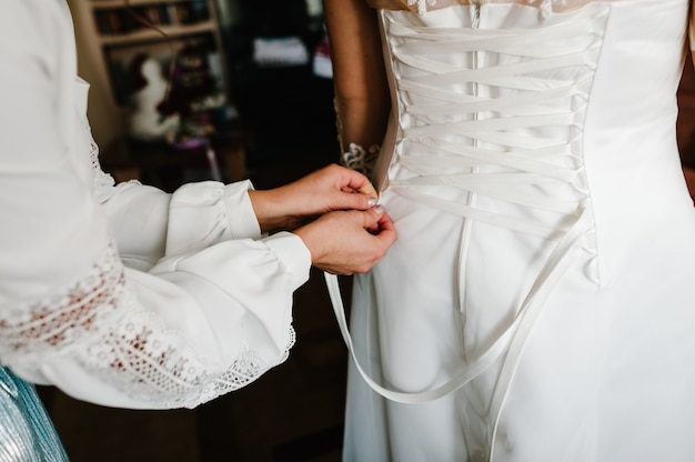 Dama de honra ajudando a noiva a apertar o espartilho e recebendo seu vestido, preparando a noiva pela manhã para o dia do casamento