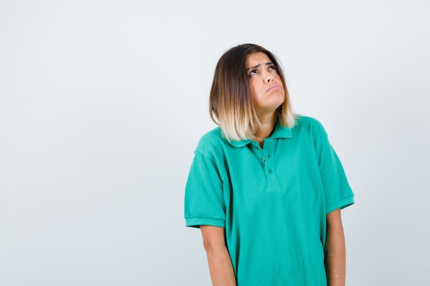 Dama elegante mirando hacia arriba con una camiseta de polo y mirando desorientada. vista frontal.