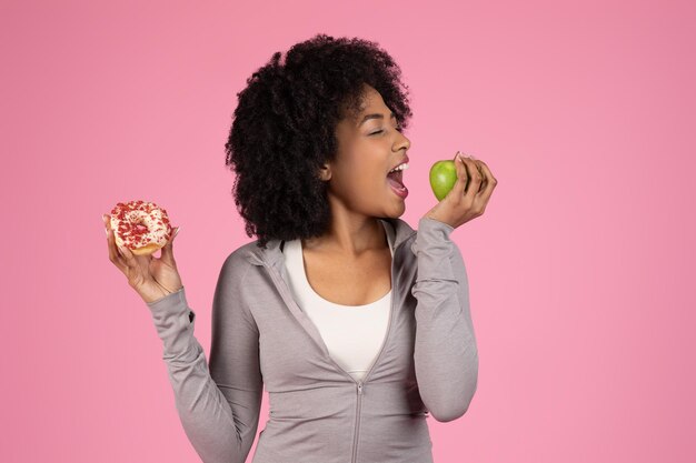 Una dama eligiendo entre una rosquilla y una manzana sobre un fondo rosa