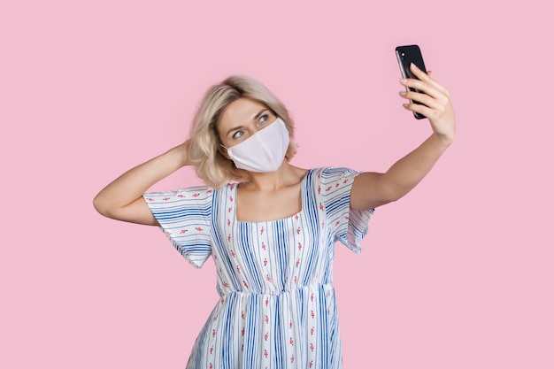 dama está haciendo un selfie en una pared rosa mientras usa una máscara