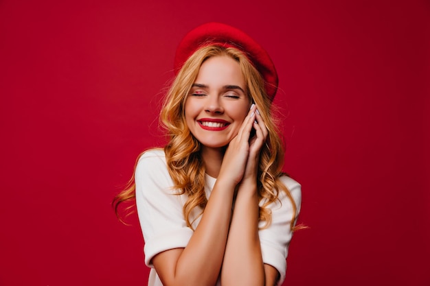 Dama francesa de ensueño posando con una hermosa sonrisa Captura interior de una mujer rubia extasiada aislada en un fondo rojo