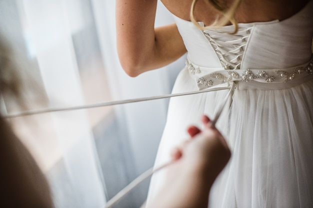 La dama de honor ayuda a vestir un vestido de novia.