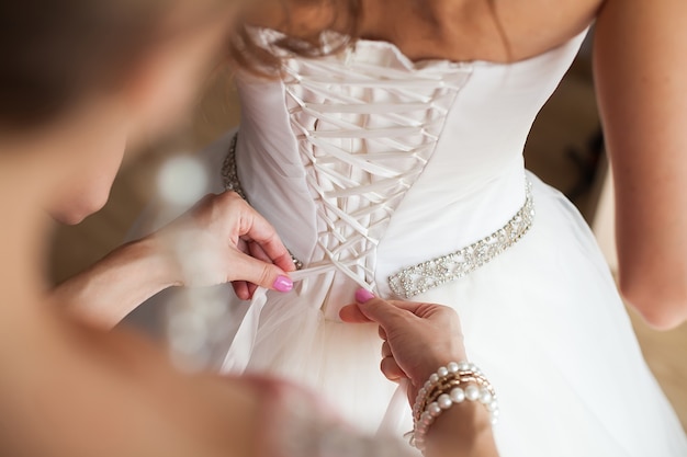 La dama de honor hace un moño en la parte posterior del vestido de novia de la novia.