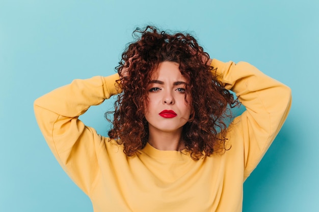 La dama con lápiz labial rojo desarregló el cabello rizado Retrato de mujer de ojos azules en suéter amarillo sobre fondo aislado